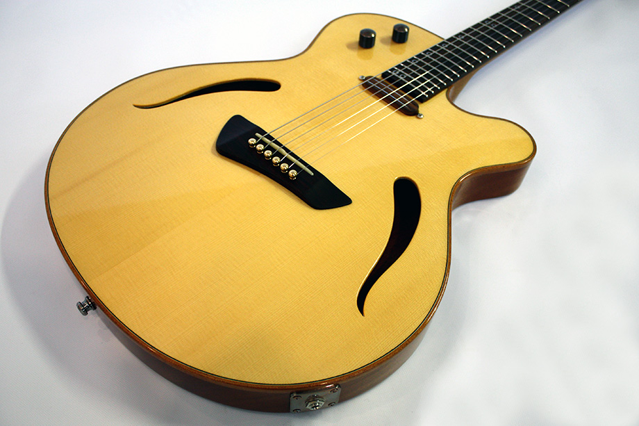 Hybrid Gitarre mit Fichtendecke, Akustikgitarrensteg und magnetischem Tonabnehmer. Decke transparent Gelb mit F-Löchern und dunklem Palisander Griffbrett.